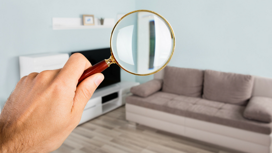 man holding magnifying glass looking at a room in an apartment